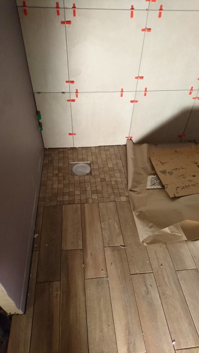 Nylagt trägolv möter kakel med distanskilar på väggen i pågående hemrenovering.