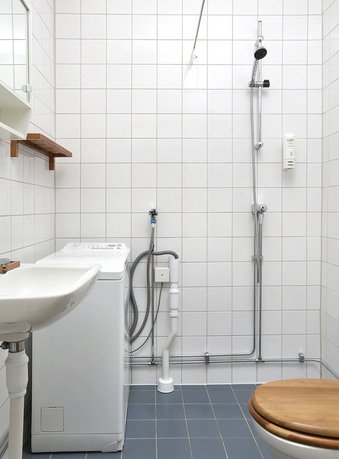 Litet badrum med kaklade väggar, tvättmaskin, handfat och dusch, eluttag nära dörrfodret.