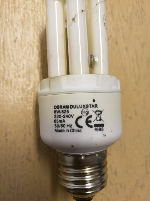 Närbild på en använd Osram Duluxstar lågenergilampa mot en vägg, märkt "Made in China".