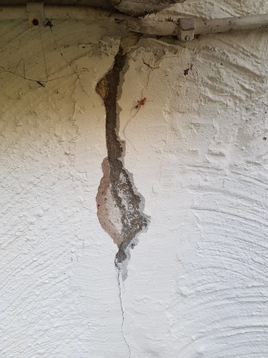 Vit putsad vägg med släppt puts och sprickbildning vid trolig skarv mellan bostad och garage.