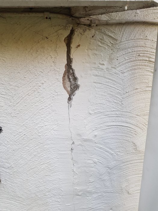 Skada i puts på vägg med synlig spricka och flagning, eventuell gammal skarv mellan bodel och garage.