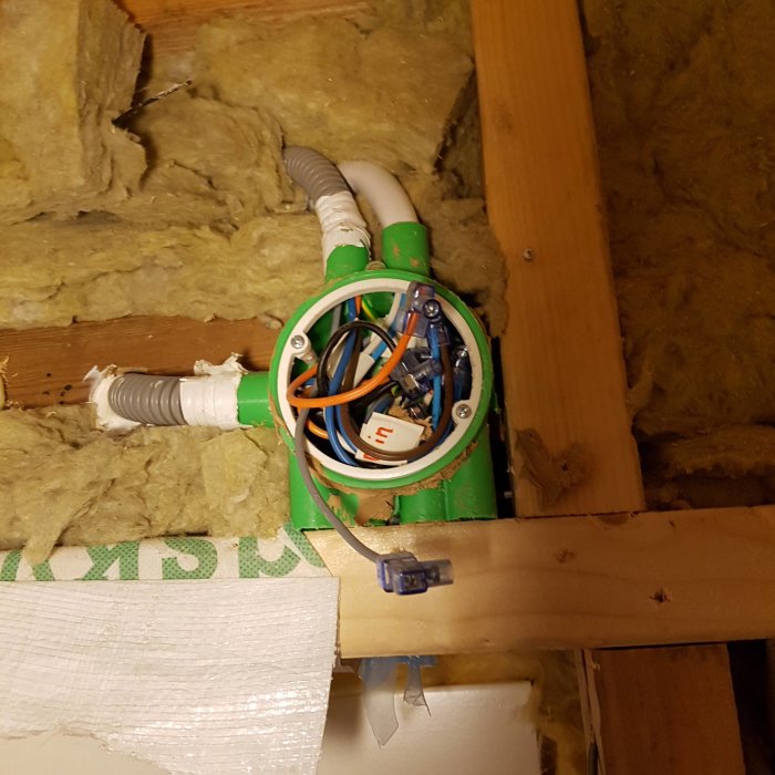 Öppen kopplingsdosa med elektriska ledningar i en isolerad väggkonstruktion.