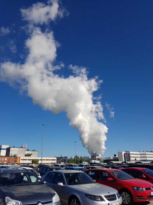 Rökpelare stiger upp över parkerade bilar mot en klarblå himmel.