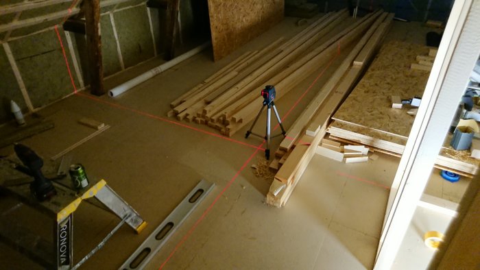 Byggplats med träreglar utlagda på golv, arbetsverktyg och laseravståndsmätare i funktion.