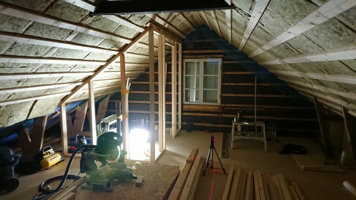 Innervägg under konstruktion med trästomme och isolering i ett vindsvåningprojekt, byggmaterial och verktyg synliga.