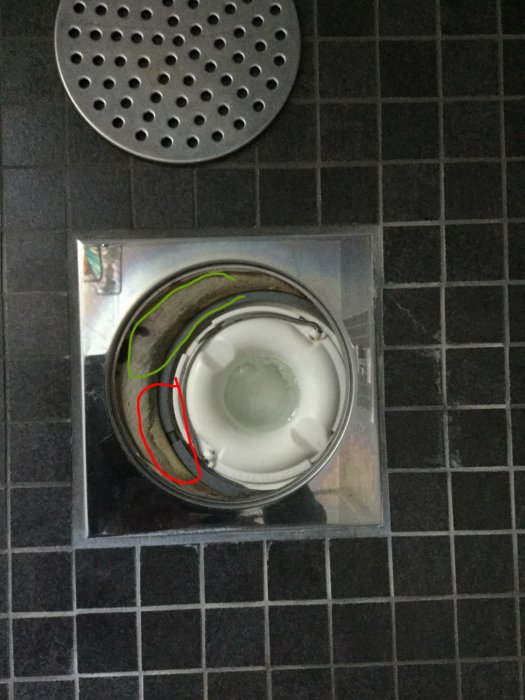 Del av ett duschkabinett med en synlig del av rött tätskikt och grönt fix på svarta kakelplattor.