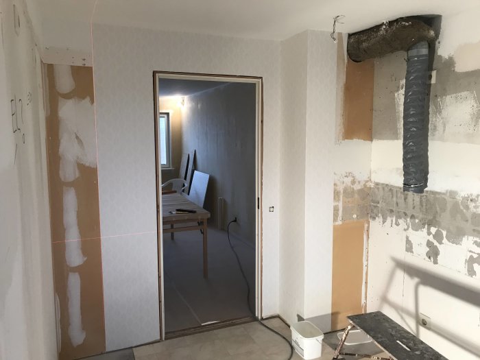 Kök under renovering med delvis tapetserade väggar och avlägsnad golvmatta.