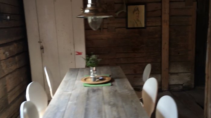 Rustikt renoverat stall med träväggar och enkelt dukat bord under hängande lampa, potentiellt för uppesittarkväll.