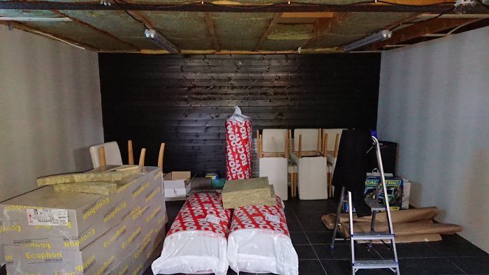 Pågående byggnation av ett hemmabiorum med svarta väggar och otillräcklig takisolering, omgivet av byggmaterial och verktyg.