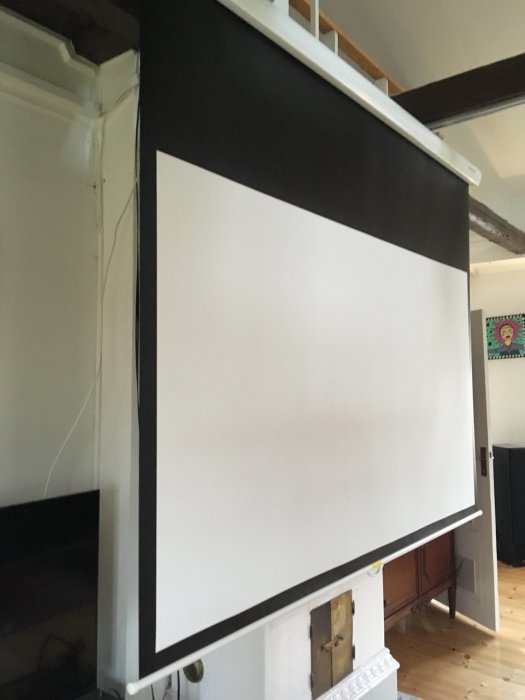 Projektorduk "Grandview Fantasy Master 100 tum" upprullad i ett vitt rum med synlig öppen spis.