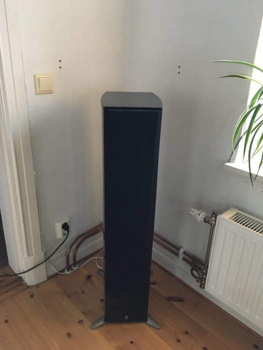En Yamaha ns-555 golvhögtalare i ett ljust rum med trägolv och radiator.