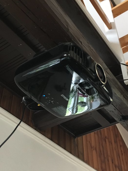 En EPSON EH-TW6000-projektor monterad i taket i ett rum med träpanel och en öppen dörr.