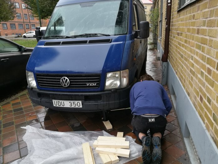 Person i arbetskläder fixar en blå VW Transporter parkerad på en gata.