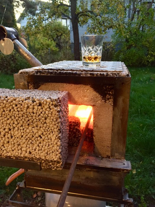 Ett glas med sprit på toppen av en tänd smedja omgiven av grönska.