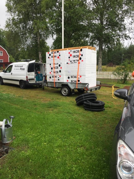 Lastad släpvagn med cellplastisolering vid byggarbetsplats under molnig himmel.