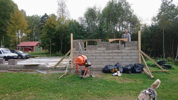 Halvfärdigt garage med murade väggar, gjuten platta, betongblandare och person som arbetar.