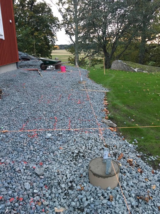 Byggplats med makadamgrund, riktsnören, utmärkta områden med märkspray och en gjuten betongplint.