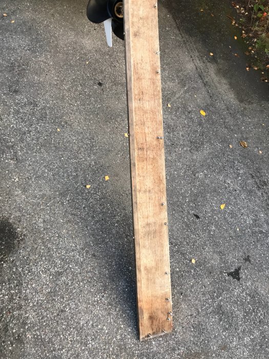 Ekplywood med skruvhål, använt som kapellfäste på båt, ligger på asfalt.