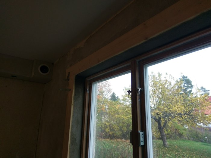Nyligen putsad fönstersmyg runt ett fönster med träram och utsikt över träd.