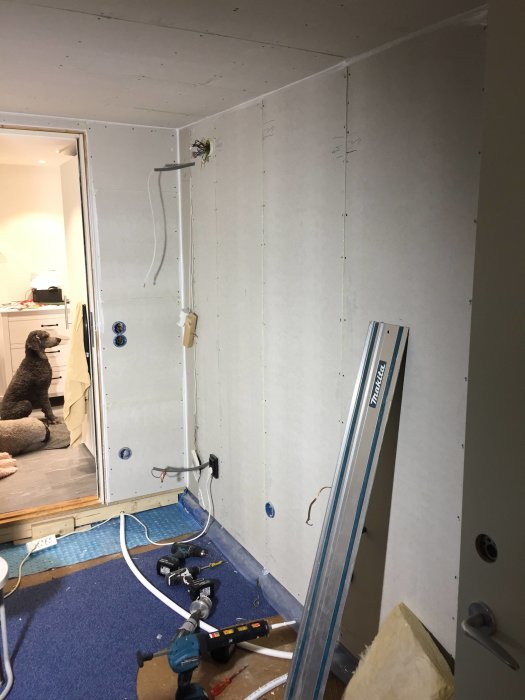 Renoveringsarbete med nya gipsskivor installerade på en vägg och verktyg på golvet.