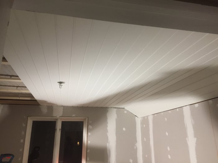 Delvis installerat vitt innertak med synliga skarvar och ojämna väggar.