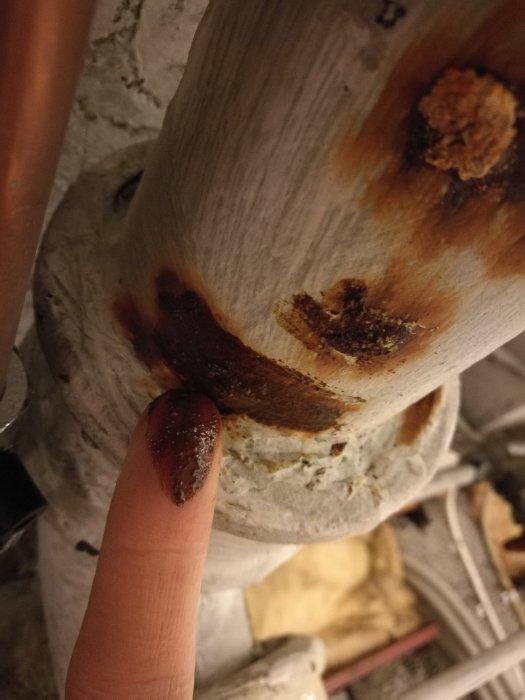 Finger som pekar på rostiga vårtor på en gammal gjutjärnsavloppsrör i en källare.