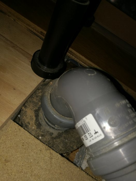 Horisontellt avloppsrör i gjutjärn med rostiga, fuktiga "vårtor" i en källare, synlig anslutning till PVC-rör.