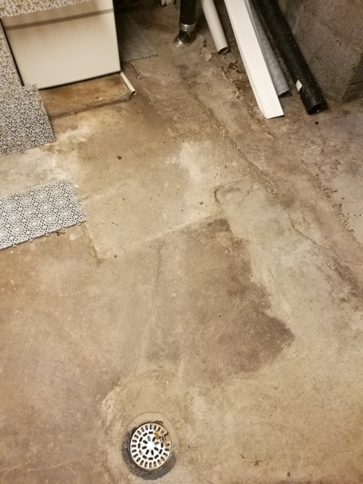 Grov betonggolv med avloppsbrunn och synligt svart avloppsrör i höger överkant.