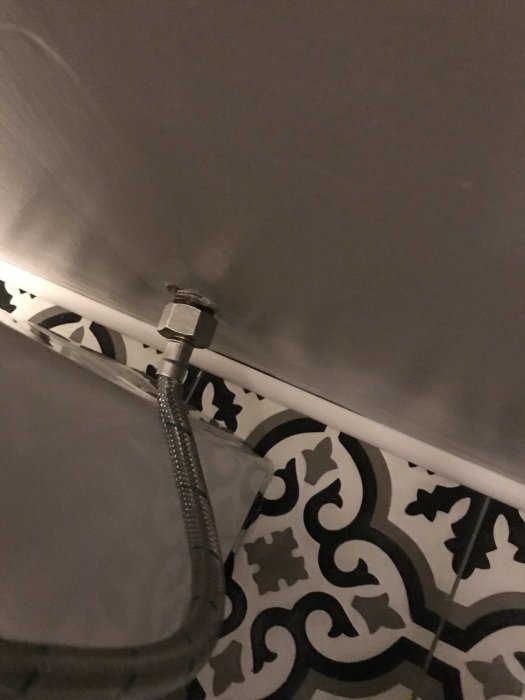 Toalettrör utan vinklad koppling intill väggen på ett mönstrat golv.