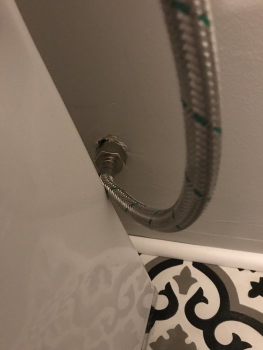 Vattenledning utan vinklad koppling går in i väggen bredvid toaletten.