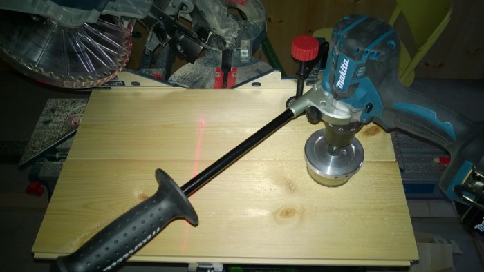 Ett hål borrats i två sammanfogade träbrädor med en handöverfräs och en laserlinje markerar rätt position.