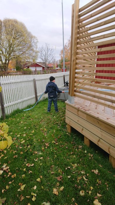 Barn hjälper till med trädgårdsarbete, dränerar vatten med en slang nära en träkonstruktion och gräsmatta med löv.