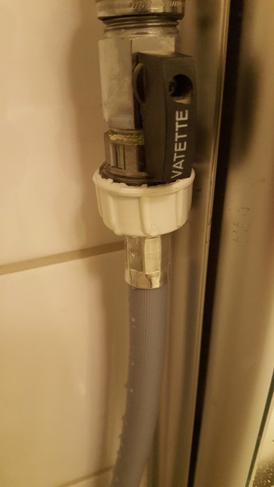 Anslutningsslang till en tvättmaskin med vattendroppar vid kopplingen, indikerar läckage.