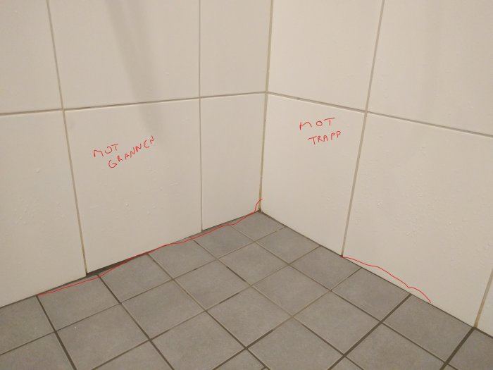 Sprickor i grå klinker på badrumsgolv längst en rad närmast väggen, indikerat med röd linje.