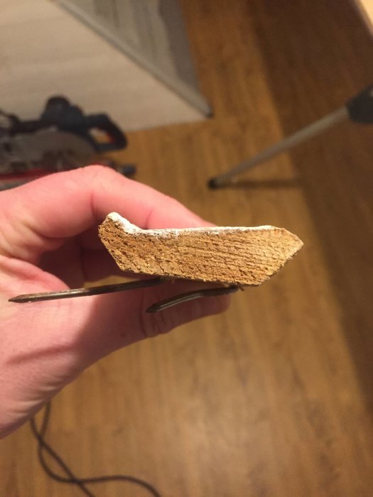 Hand håller en gammal, sprucken taklist med flera lager knottrig färg.