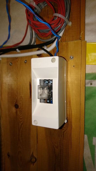 Inkapsling monterad på vägg med en liten svart wallswitch och ett relä inuti, kopplat till flera kablar.