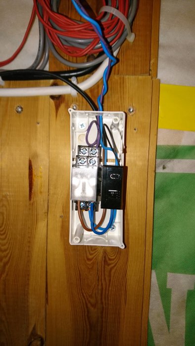 Wallswitch och relä installerade i inkapsling på trävägg, anslutna till kablar för styrning av värmesystem.