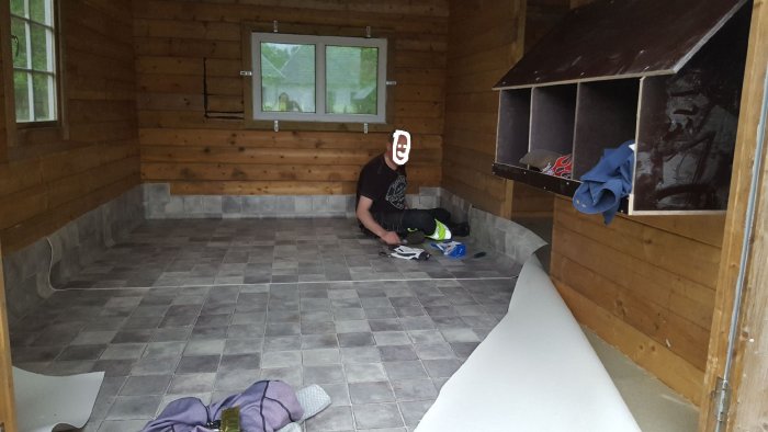 Person lägger in matta i ett hönshus med trätak och väggar och en vägg med värpreden.