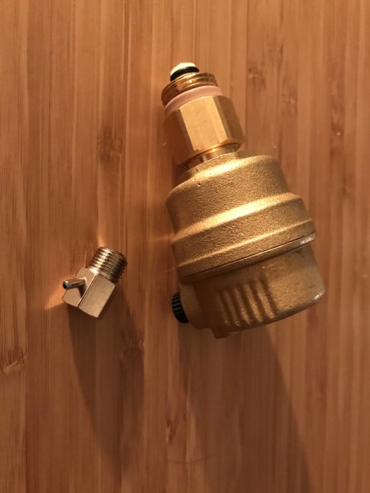 Närbild av en ny avluftare och en luftskruv mot träbakgrund i samband med byte på värmepump.