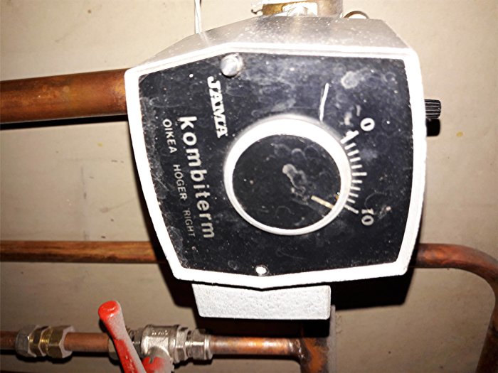 Upside-down view of a manual temperature controller with dial, labeled in Finnish, attached to copper piping, indicating max setting.