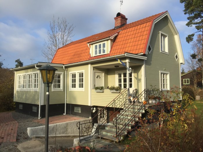 Renoverat traditionellt hus i ljus färg med tegeltak, veranda och trädgårdslampa under dagtid.