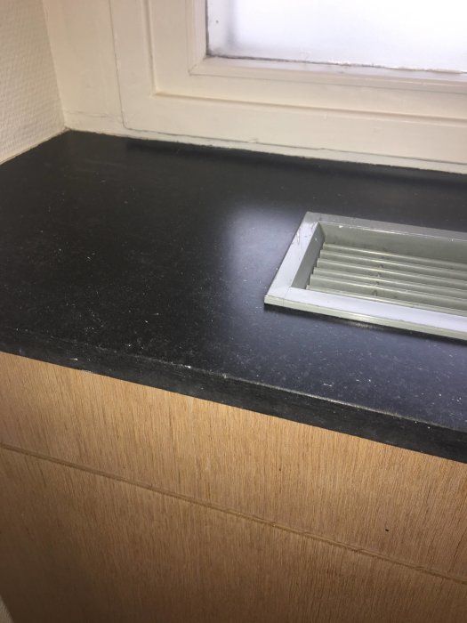 Svart fönsterbänk som misstänks vara Eternitskiva, nära ett fönster med vit karm.