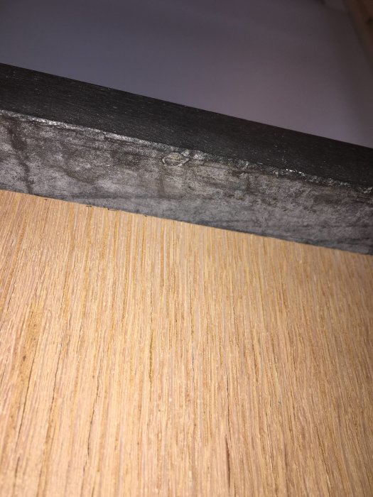 Närbild på misstänkt Eternitskiva som används som fönsterbräda mot trästrukturerad yta.