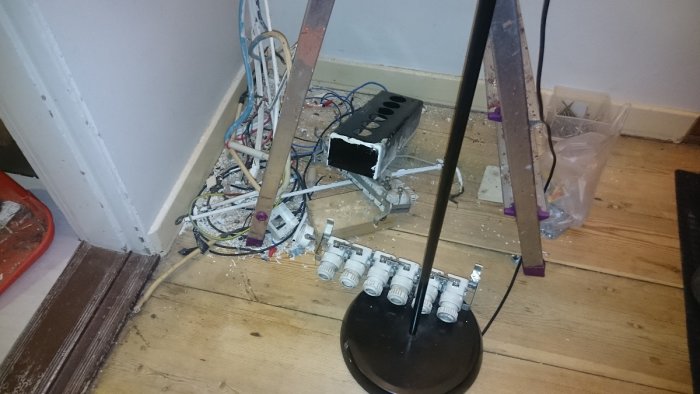 Rörigt hörn av ett rum med öppen elinstallation, kablar och avtaget golvsockel under renovering.