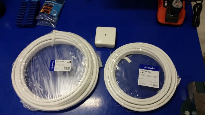 Verktyg och material för elinstallation: kablar, kopplingsdosa, pluggar, skruvdragare på blå bakgrund.
