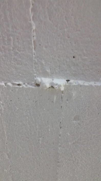 Nahaufnahme einer Wand mit einer sichtbaren Rissbildung und Spachtelmasse entlang der Risskante.