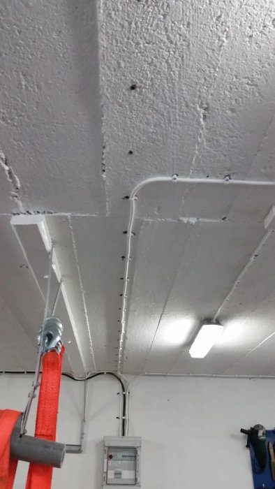 Vit källartak med synliga kablar och en elektrisk central samt en hängande lampa.