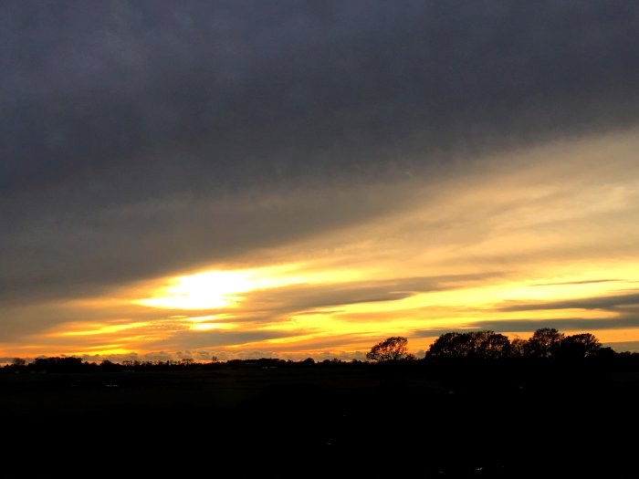 Solnedgång med dramatiska moln och gyllene himmel över ett landskap.