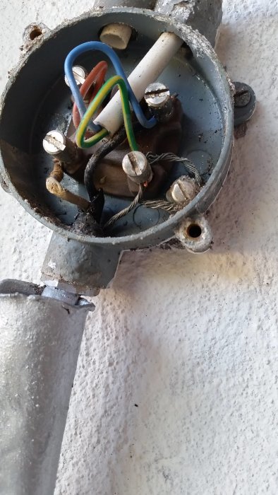 En öppen eldosa med äldre färgade elledningar och anslutna skruvkontakter.