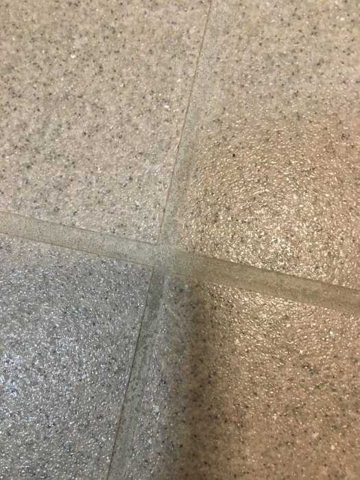 Fläckiga och missfärgade fogar mellan ljusa klinkerplattor på ett badrumsgolv.